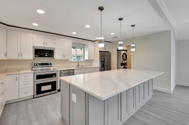 kitchen with a kitchen island, stainless steel appliances, sink, white cabinetry, and light stone counters