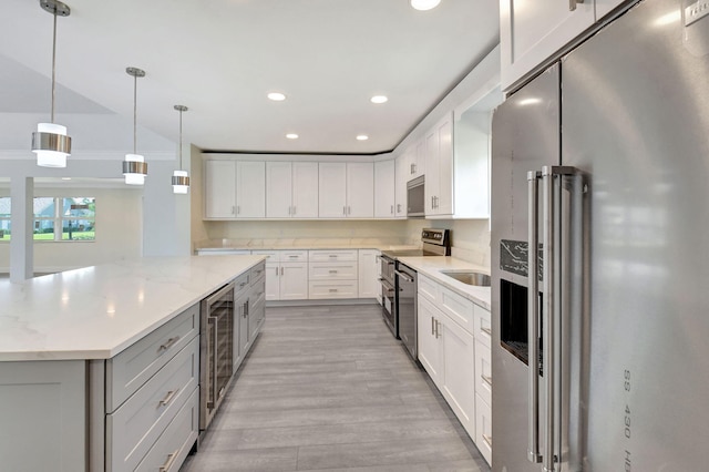 kitchen featuring white cabinets, beverage cooler, light stone counters, pendant lighting, and stainless steel appliances