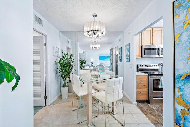 kitchen featuring light brown cabinetry, appliances with stainless steel finishes, a textured ceiling, pendant lighting, and an inviting chandelier