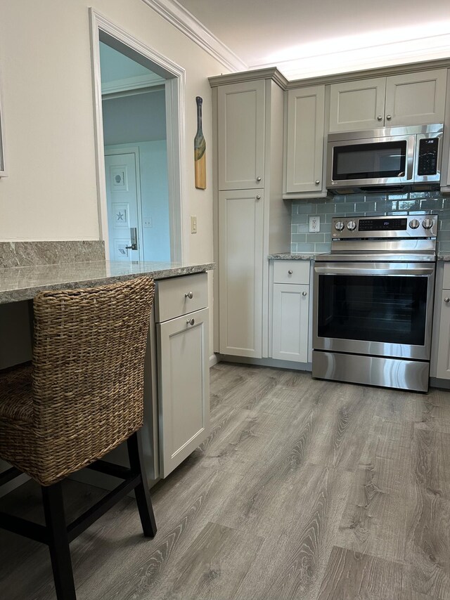 kitchen with appliances with stainless steel finishes, backsplash, light stone counters, crown molding, and light hardwood / wood-style flooring