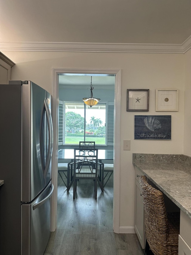 kitchen with pendant lighting, dark wood-type flooring, crown molding, stainless steel fridge, and light stone countertops