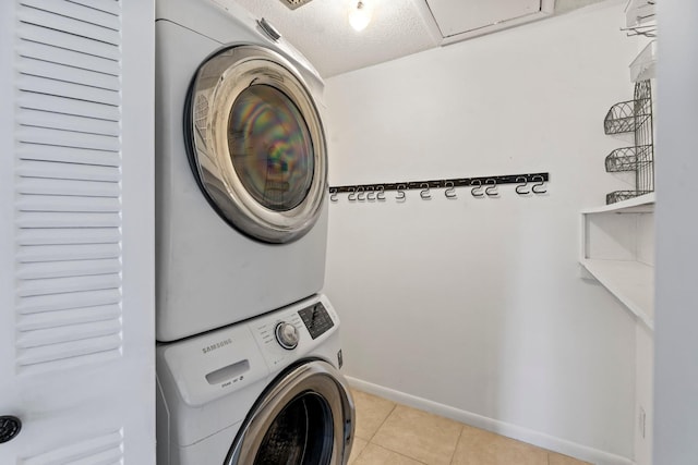 laundry room featuring a textured ceiling, light tile patterned flooring, and stacked washer and clothes dryer