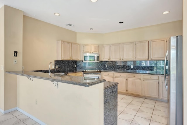 kitchen with appliances with stainless steel finishes, sink, kitchen peninsula, dark stone counters, and decorative backsplash