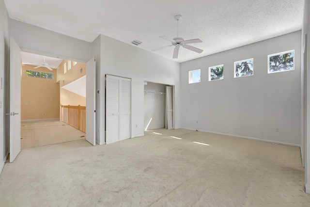 unfurnished bedroom featuring light carpet, a textured ceiling, multiple closets, and ceiling fan