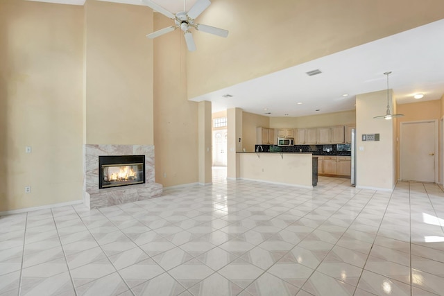 unfurnished living room featuring a multi sided fireplace, ceiling fan, a towering ceiling, and light tile patterned floors