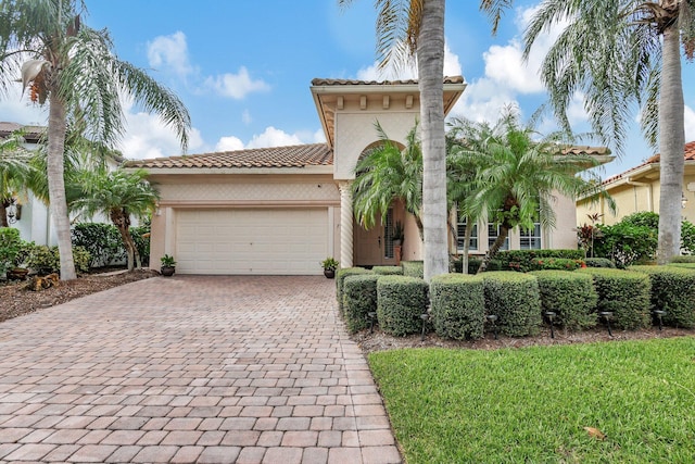 mediterranean / spanish-style house with stucco siding, a tiled roof, decorative driveway, and a garage