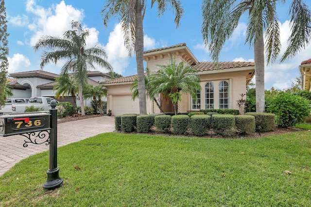 mediterranean / spanish-style home with an attached garage, stucco siding, a front lawn, a tiled roof, and decorative driveway