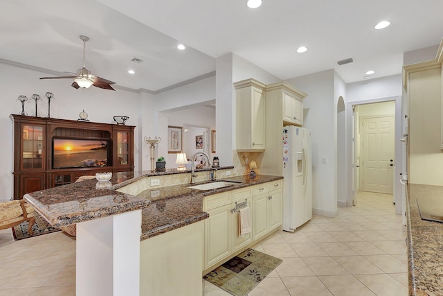 kitchen with dark stone countertops, white fridge with ice dispenser, and cream cabinetry