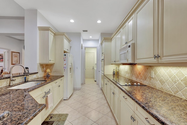 kitchen featuring white appliances, dark stone countertops, cream cabinets, and sink