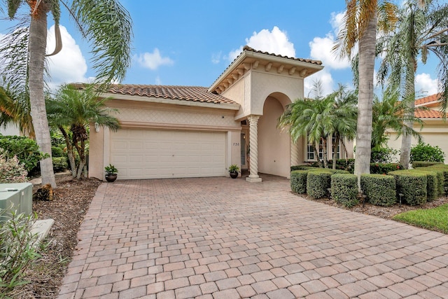 mediterranean / spanish-style home featuring a tiled roof, stucco siding, an attached garage, and decorative driveway