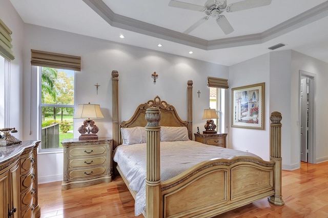 bedroom featuring ceiling fan, a tray ceiling, multiple windows, and light wood-type flooring