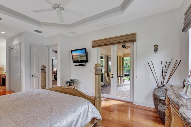 bedroom featuring light hardwood / wood-style floors, access to outside, a tray ceiling, and ceiling fan