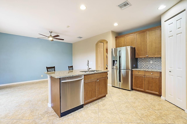 kitchen featuring light stone countertops, appliances with stainless steel finishes, an island with sink, sink, and backsplash