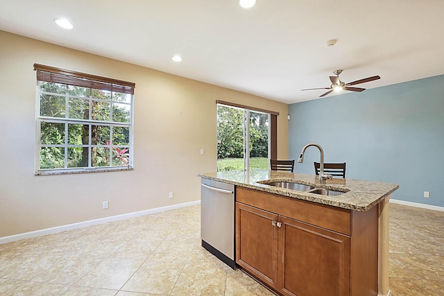 kitchen with ceiling fan, sink, light stone counters, stainless steel dishwasher, and a center island with sink