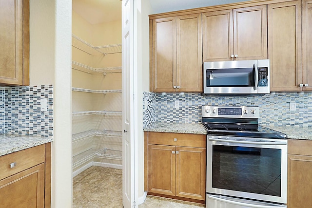 kitchen featuring decorative backsplash, light stone countertops, appliances with stainless steel finishes, and light tile patterned floors