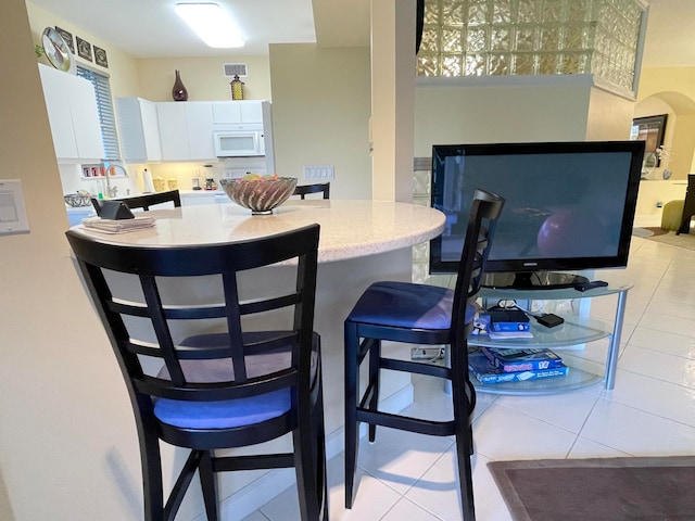 interior space featuring a breakfast bar area, white cabinetry, and light tile patterned floors