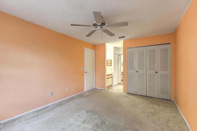 unfurnished bedroom featuring ceiling fan, light colored carpet, a textured ceiling, and ensuite bathroom