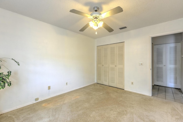 unfurnished bedroom with ceiling fan, a closet, light carpet, and a textured ceiling