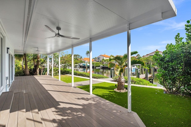 wooden deck featuring a lawn, ceiling fan, a water view, and a boat dock