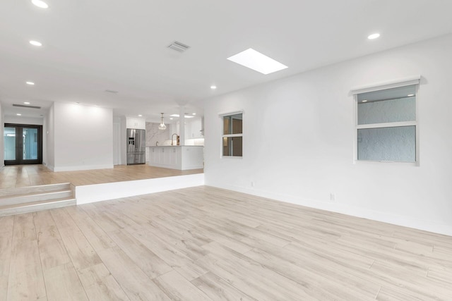 unfurnished living room featuring a skylight, light hardwood / wood-style flooring, and sink