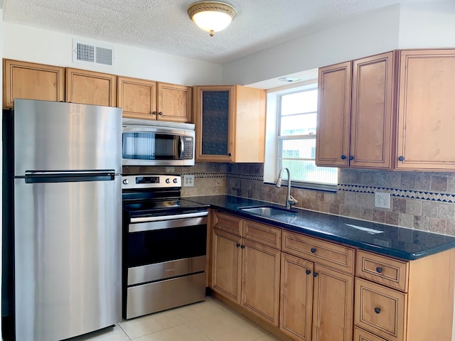 kitchen with appliances with stainless steel finishes, sink, a textured ceiling, decorative backsplash, and light tile patterned floors