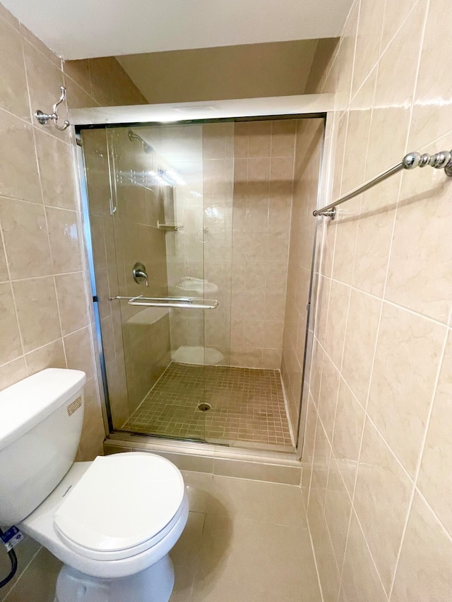 bathroom featuring toilet, a shower with shower door, tile patterned floors, and tile walls