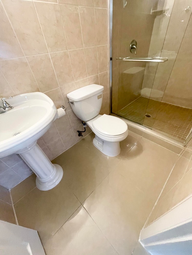 bathroom featuring toilet, tile patterned flooring, sink, tile walls, and an enclosed shower