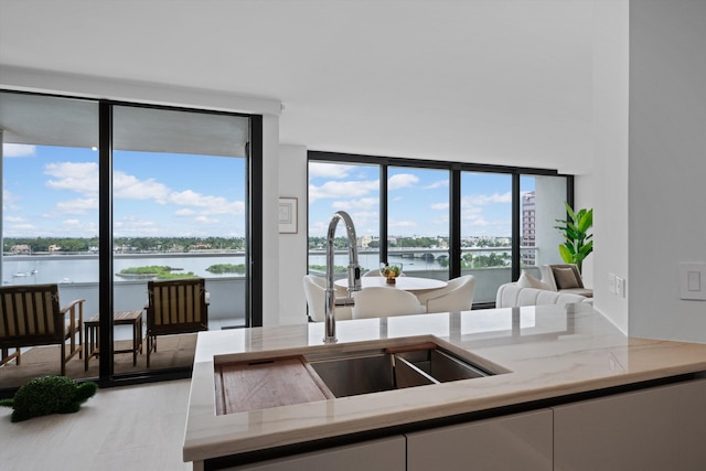 kitchen featuring white cabinetry, floor to ceiling windows, light hardwood / wood-style floors, sink, and a water view