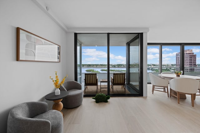 living area featuring a wealth of natural light, light hardwood / wood-style flooring, a water view, and floor to ceiling windows