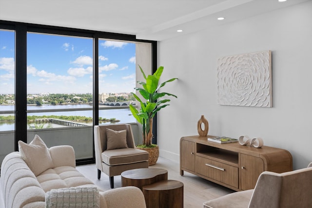 sitting room with expansive windows, light hardwood / wood-style flooring, and a water view