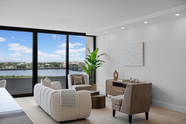 living room with light hardwood / wood-style floors, a wall of windows, and a water view