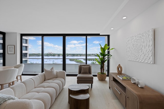 living room with a wealth of natural light, a water view, light wood-type flooring, and floor to ceiling windows