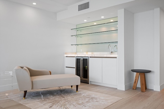 bar with wine cooler, light wood-type flooring, and white cabinets