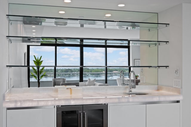 bar featuring sink, light stone countertops, beverage cooler, white cabinets, and a water view