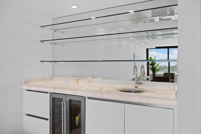 bar with wine cooler, sink, white refrigerator, white cabinets, and light stone counters