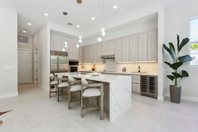 kitchen featuring pendant lighting, a kitchen island with sink, beverage cooler, light stone counters, and extractor fan