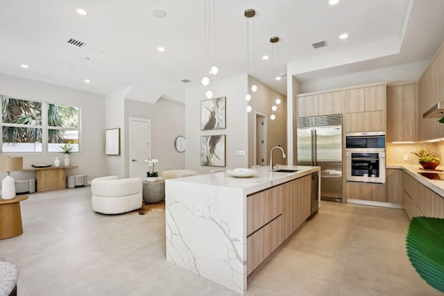 kitchen featuring appliances with stainless steel finishes, backsplash, a kitchen island with sink, sink, and hanging light fixtures