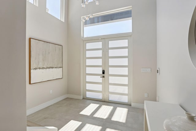 carpeted entrance foyer featuring baseboards, french doors, and a towering ceiling