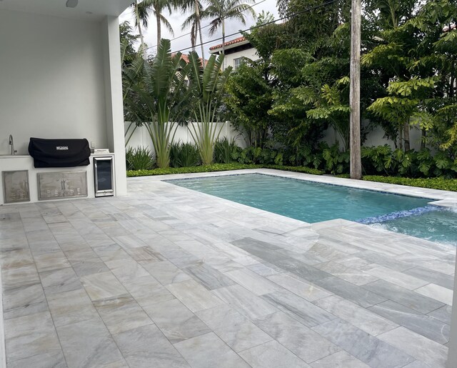 view of swimming pool with an outdoor kitchen, a patio, fence, and a pool with connected hot tub