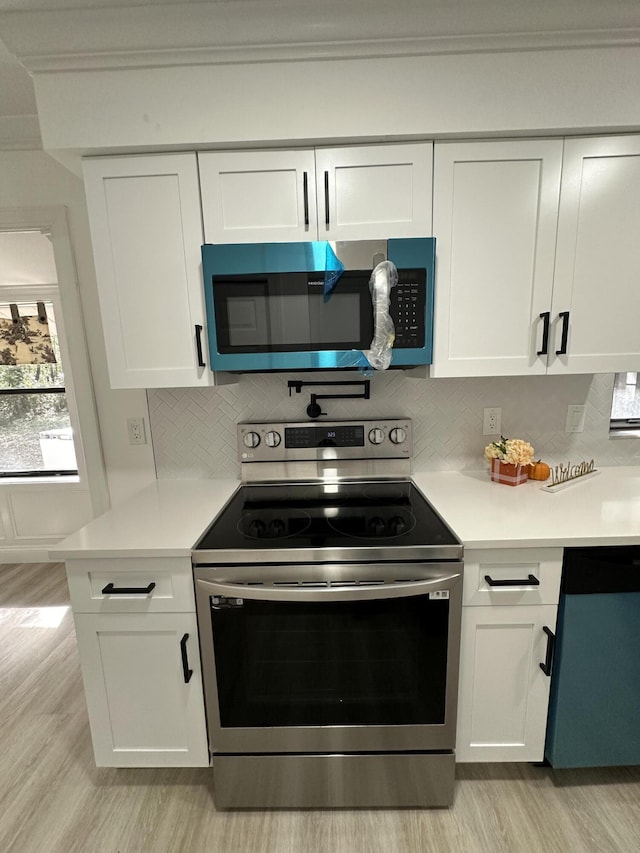 kitchen with appliances with stainless steel finishes, light hardwood / wood-style flooring, white cabinets, and backsplash