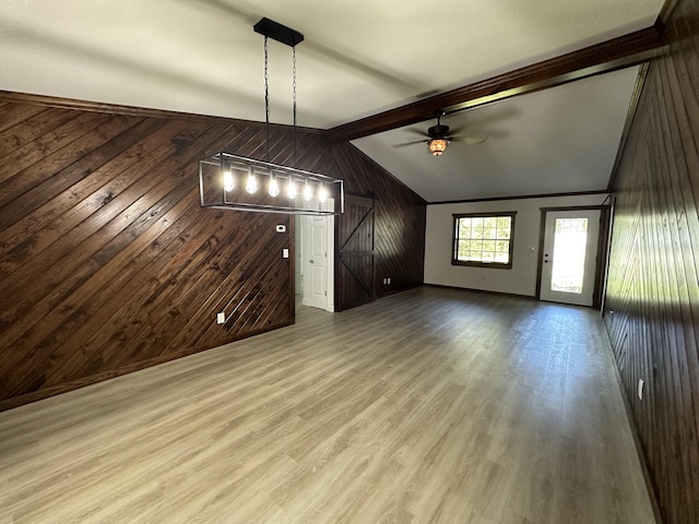 unfurnished living room with a barn door, wood-type flooring, vaulted ceiling with beams, ceiling fan, and wooden walls