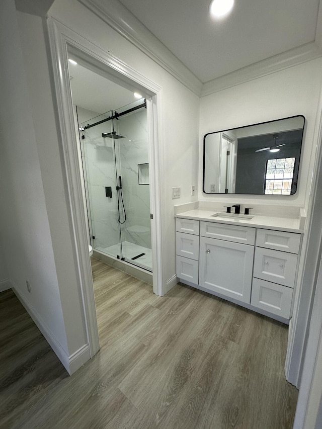 bathroom featuring a shower with door, crown molding, ceiling fan, wood-type flooring, and vanity