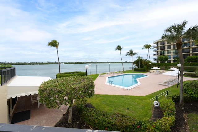 view of swimming pool featuring a patio area, a water view, and a lawn