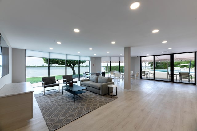 living room with expansive windows, a water view, and light wood-type flooring