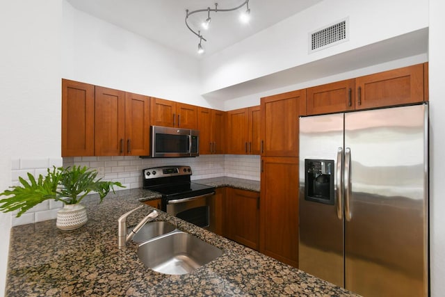 kitchen with appliances with stainless steel finishes, tasteful backsplash, dark stone countertops, and sink