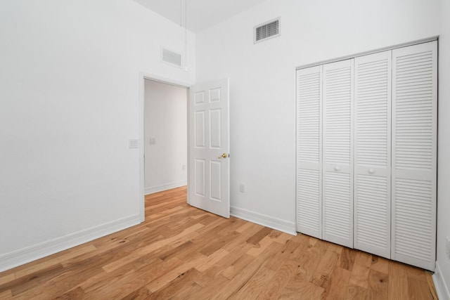 unfurnished bedroom featuring light wood-type flooring, a high ceiling, and a closet