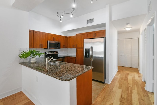 kitchen with dark stone counters, sink, light wood-type flooring, appliances with stainless steel finishes, and kitchen peninsula