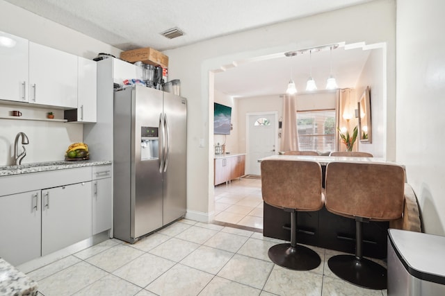 kitchen featuring hanging light fixtures, sink, stainless steel fridge, light tile patterned floors, and white cabinets