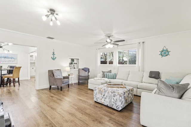 living room featuring hardwood / wood-style floors, ceiling fan with notable chandelier, and ornamental molding