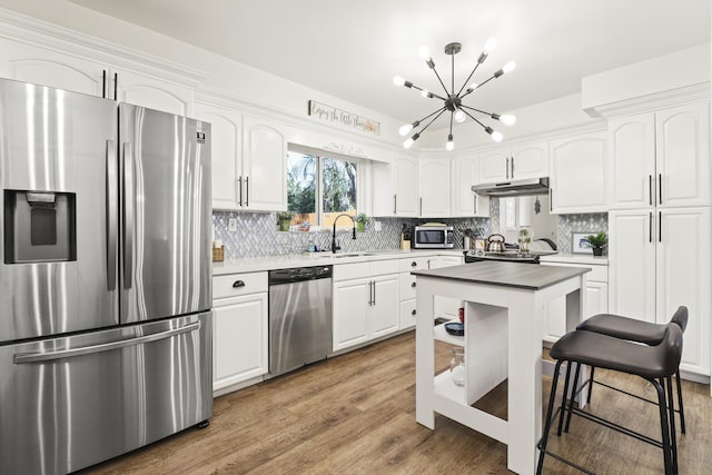 kitchen with appliances with stainless steel finishes, sink, white cabinets, backsplash, and hardwood / wood-style flooring